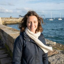 Maren Holt smiling outdoors on a breezy harbour wall